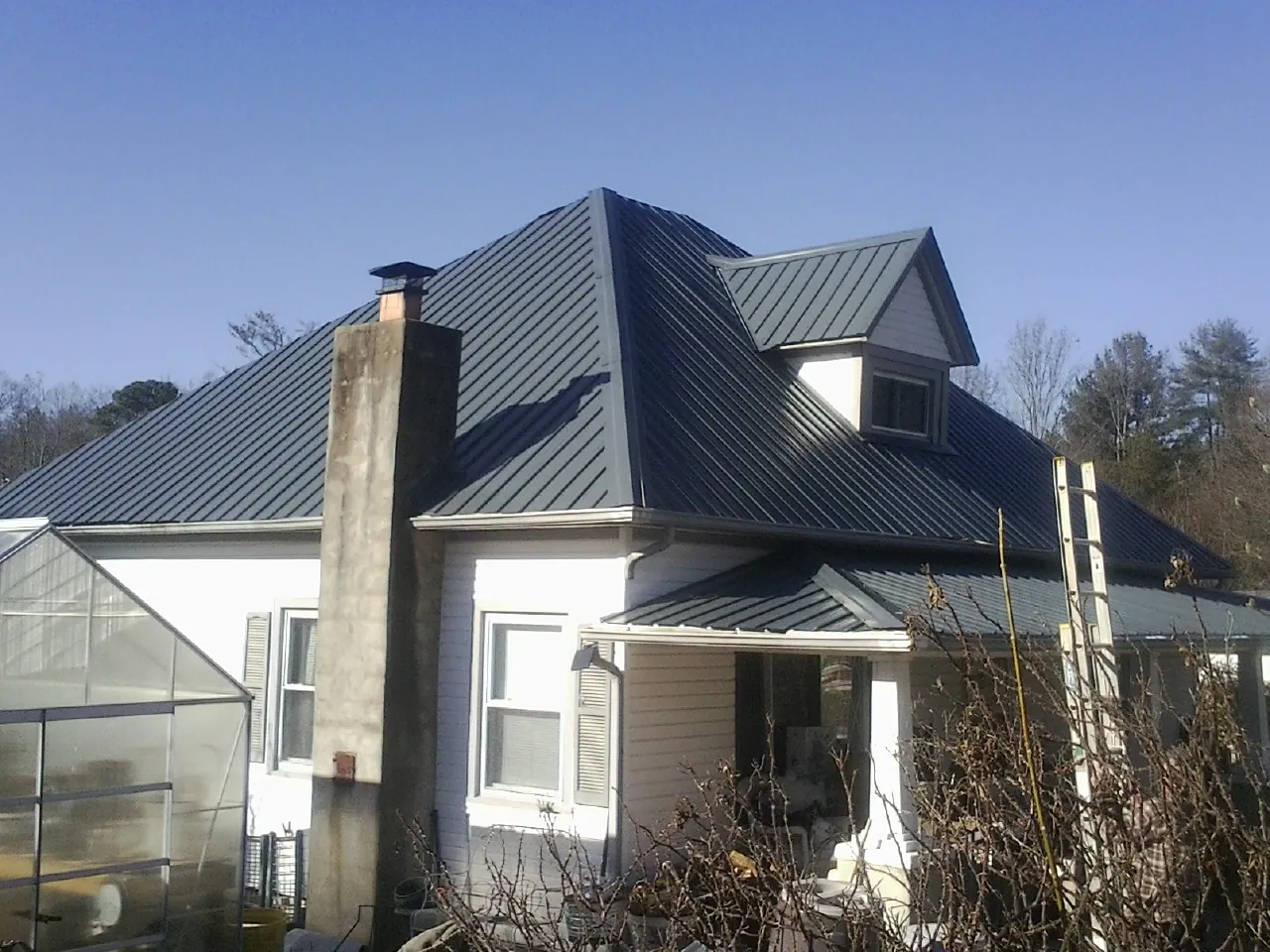 Dark blue standing seam metal roof on a white farmhouse with dormer — Slate & Tile Roof Repair by Roofing Brothers in Wapello