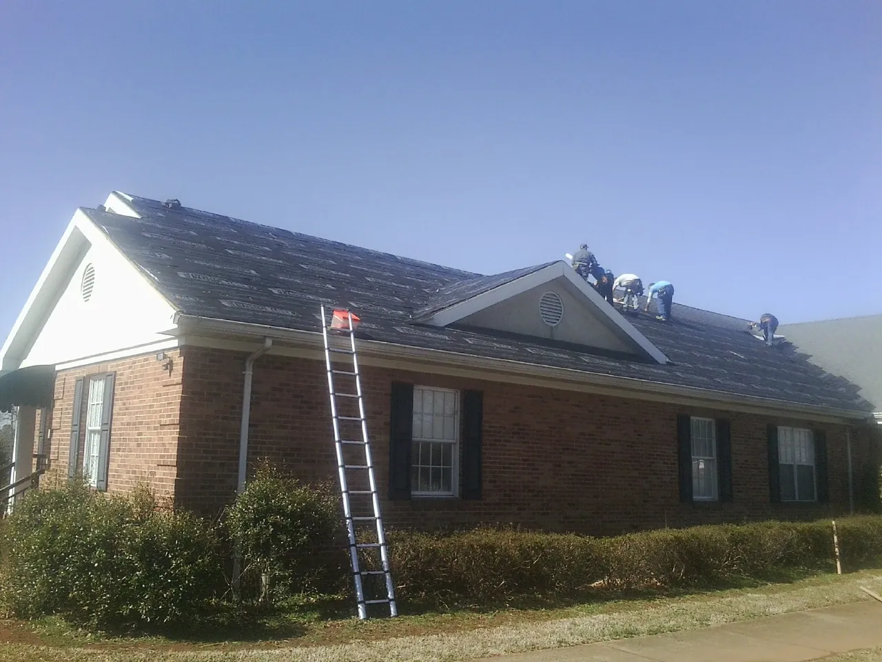 Crew tearing shingles off a brick ranch roof with a ladder set — Metal Roof Repair work by our crew in Wapello
