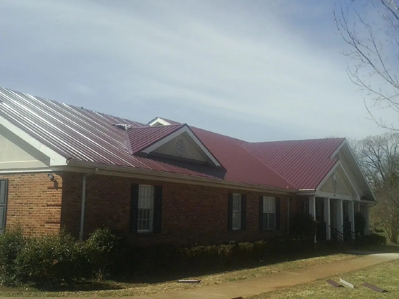 Red metal roof with gabled entries on a long brick building, from a Hail Damage Roof Repair job in Wapello