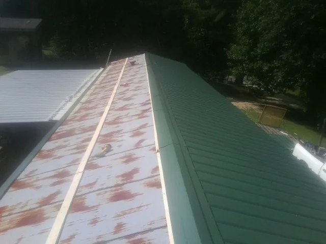 Old rusted panels beside newly installed green metal roofing — Wind Damage Roof Repair by Roofing Brothers in Wapello