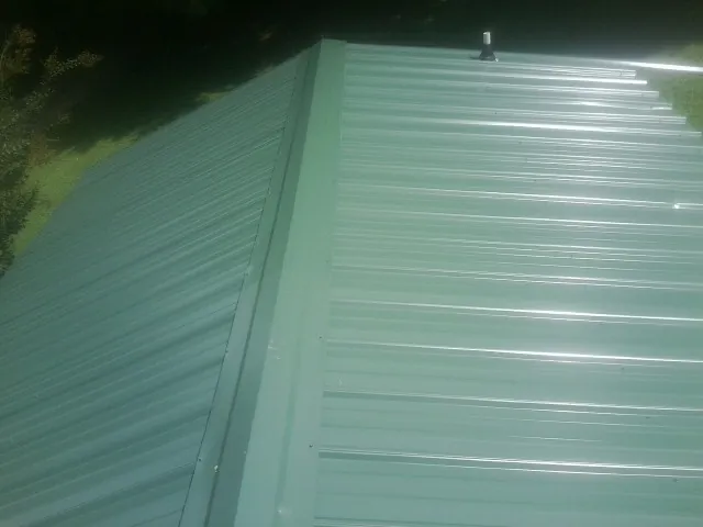 New green metal panels meeting at the ridge of a roof — Flat Roof Repair work by our crew in Wapello