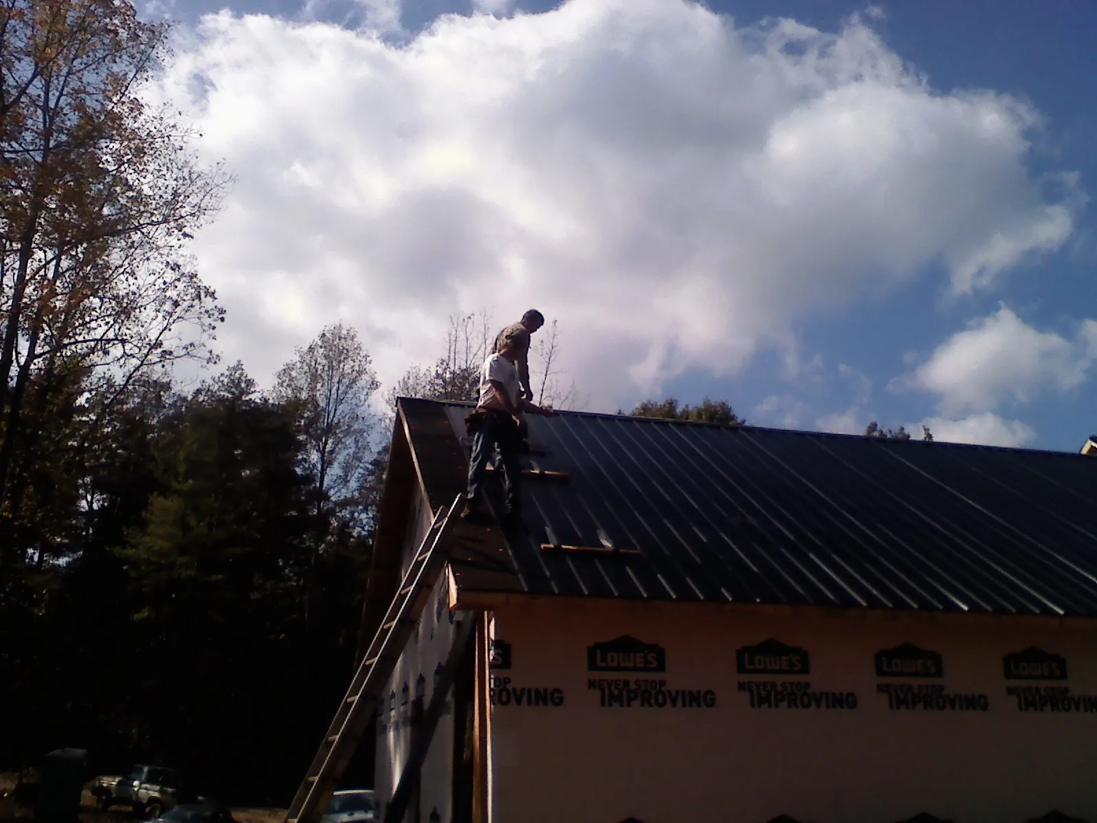 Roofer fastening dark metal panels high against a cloudy sky, from a Roof Inspection job in Wapello