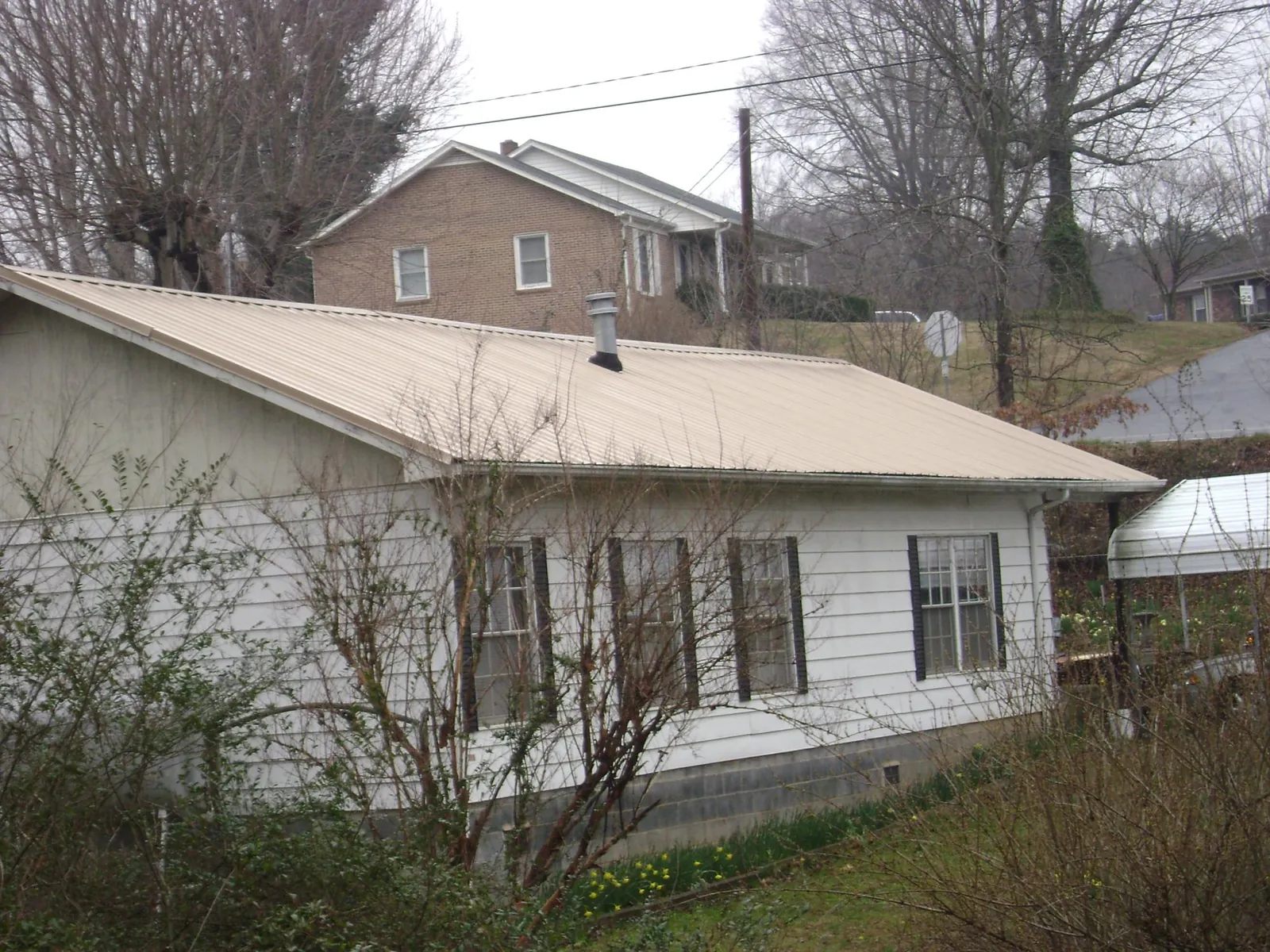 Tan metal roof on a white sided house set into a hillside — Commercial Roofing by Roofing Brothers in Wapello