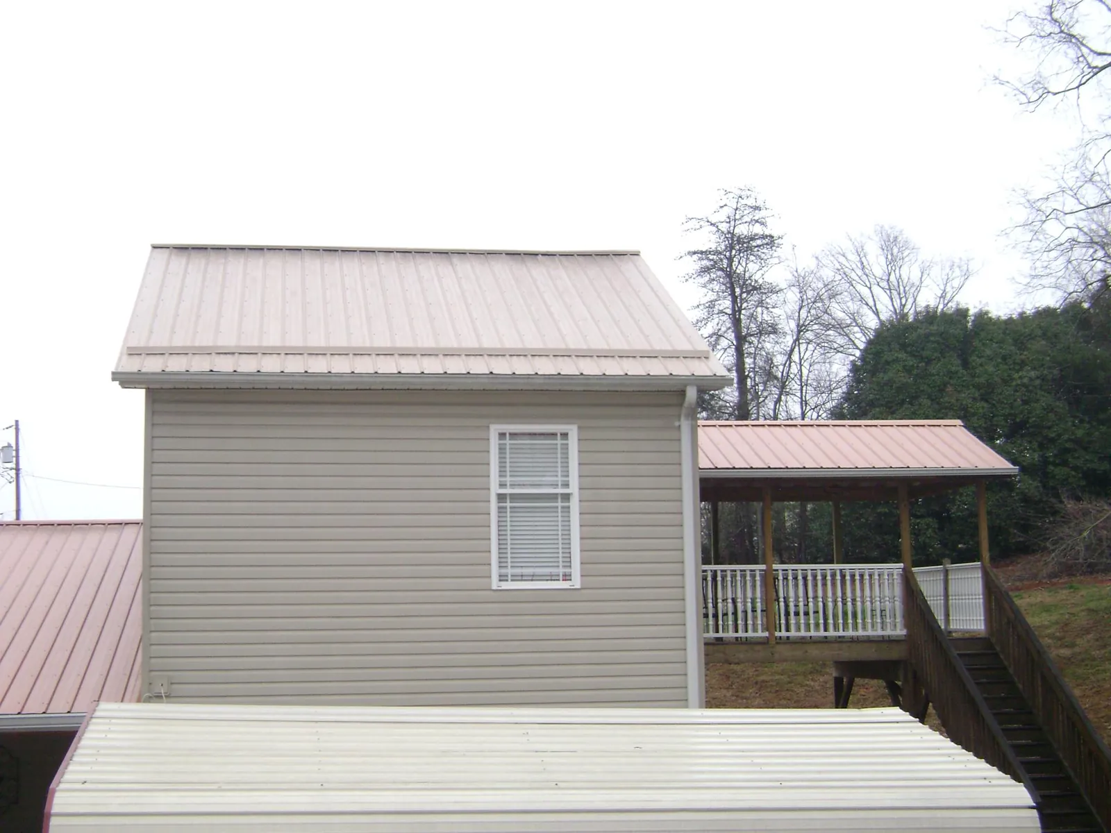 Tan metal roofs on a two story addition and attached porch, from a Roof Replacement job in Wapello
